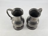 pair of silver plated jugs with handles on a white surface