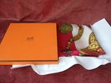 une boîte orange posée sur un tissu blanc, à côté d'un coussin rouge