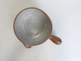 a small brown bowl with a wooden handle on a white surface