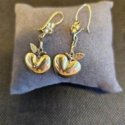 boucles d'oreilles en forme de pomme, en argent et en or, posées sur un coussin gris