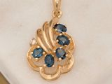 an image of a gold pendant with blue sapphires on a marble surface