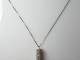 un collier en argent orné d'un pendentif carré auquel est suspendu un pompon