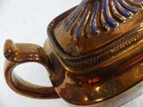 a gold teapot with a blue handle on a white table