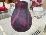 un vase violet posé sur une table dans une pièce où se trouvent d'autres vases