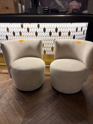 two beige chairs sitting on top of a wooden floor next to a bar