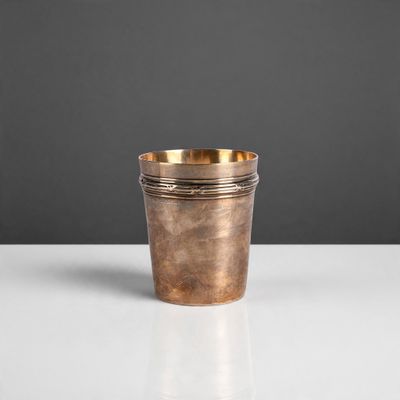 une petite tasse en cuivre posée sur une table blanche, sur fond gris