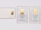 two gold bars and a piece of gold on a white surface
