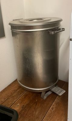une grande casserole en métal posée sur un plancher en bois, à côté d'un réfrigérateur