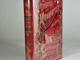 an old book with a red cover sitting on top of a white table
