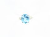 une bague avec une topaze bleue ovale et des diamants, sur fond blanc