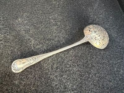 une vieille cuillère en argent avec un manche, posée sur une surface noire