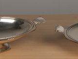 two silverplated dishes on a wooden table with a white wall in the background