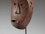 un masque en bois posé sur un socle, sur fond gris