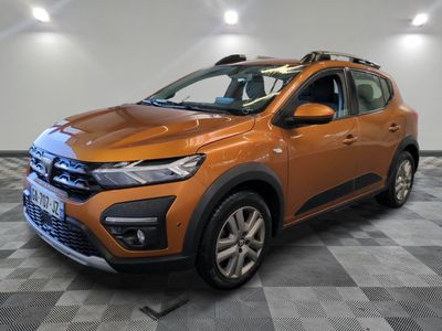 La voiture orange est garée sur un sol carrelé à damier.