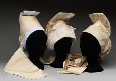 trois têtes de mannequins coiffées de chapeaux, exposées sur une surface grise