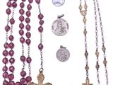 rosary, medal, and coin laying next to each other on a white surface