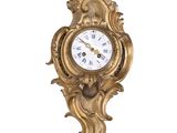 a gold clock hanging on the wall with a white background