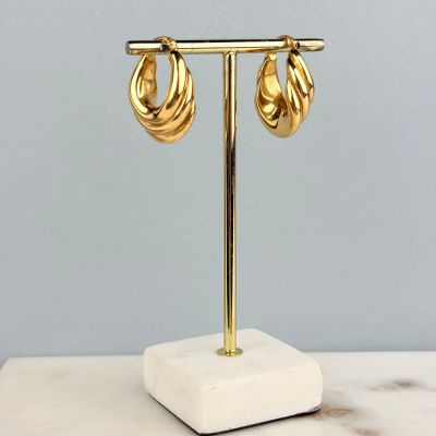une paire de boucles d'oreilles créoles plaquées or, présentées sur un socle en marbre