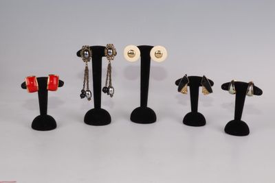 Plusieurs paires de boucles d'oreilles sont exposées sur des présentoirs noirs posés sur une surface blanche.