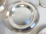 une assiette en argent posée sur une table blanche, à côté d'autres assiettes en argent