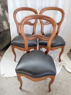 four chairs with black leather upholstered seats and a wooden frame