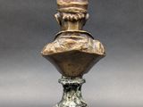 an antique bronze bust of a man with a hat on top of it
