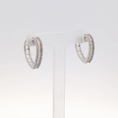 une paire de boucles d'oreilles créoles en or blanc et diamants, présentées sur un socle transparent