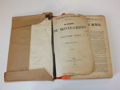 un vieux livre ouvert posé sur une table, sur laquelle se trouve un bout de papier