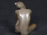 statue of a nude woman sitting on a black surface