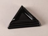 un objet en verre noir de forme triangulaire posé sur une surface blanche