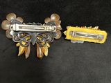two pieces of silver and yellow hair clips on a black surface