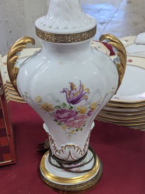 un vase blanc posé sur une table où se trouvent des assiettes et un cadre photo