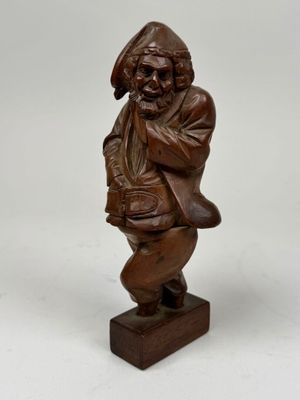 une statue en bois représentant un homme portant un chapeau et un sac