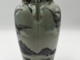a green vase with birds on it sitting on a table