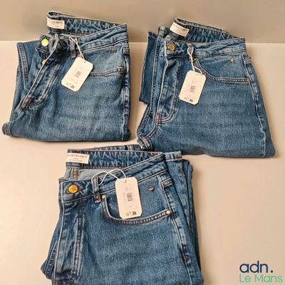 trois paires de jeans, encore étiquetées, posées sur une table