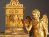 a gold statue of an angel holding a book next to a clock