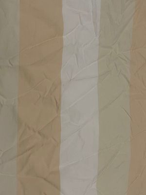 un tissu rayé beige et blanc sur un lit avec un oreiller blanc