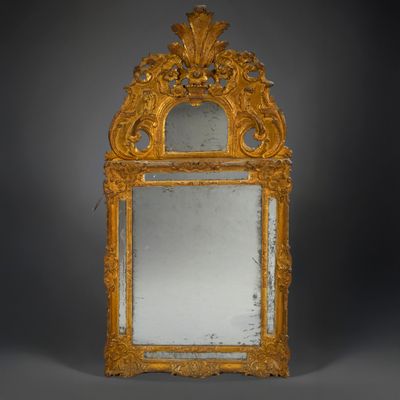 an ornately carved mirror with a gold frame on a grey background