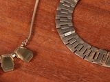 a silver necklace and a silver bracelet on a wooden table