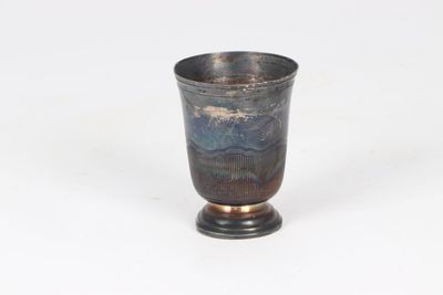 a silver cup sitting on a stand on a white surface