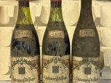 Trois bouteilles de vin sont posées sur une table devant un mur de briques.