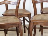 four wooden chairs with wicker seats in a row against a white wall