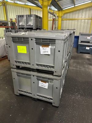 une pile de cartons dans un entrepôt, sur laquelle est accrochée une pancarte jaune