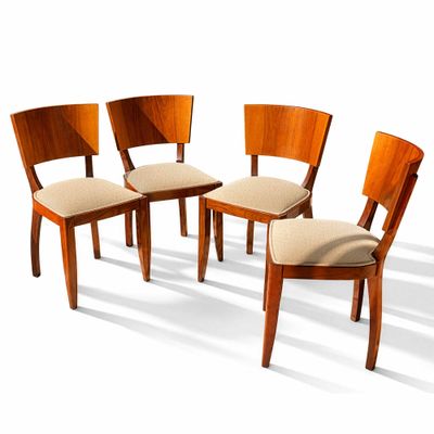 Quatre chaises en bois, dont les assises sont recouvertes d'un tissu beige, sont disposées en cercle.