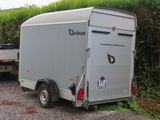 a trailer that is parked in a lot next to a bush