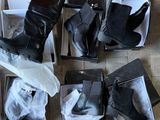 plusieurs paires de bottes noires pour femmes, dans leurs boîtes, posées sur un sol carrelé