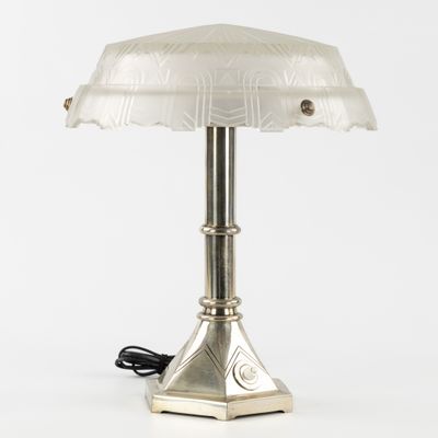 une lampe de table argentée surmontée d'un abat-jour en verre