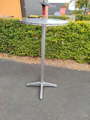 a silver table with a bird on it in front of a hedge