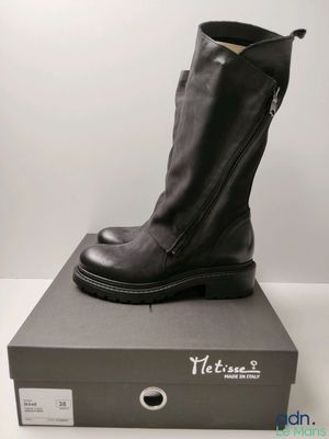 Des bottes en cuir noir avec des fermetures éclair sont posées sur une boîte