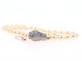 a close up of a white pearl bracelet with a diamond clasp